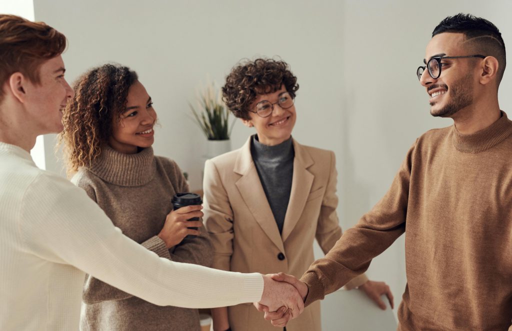 Diverse group of young adults shaking hands in an office environment, depicting teamwork and collaboration.